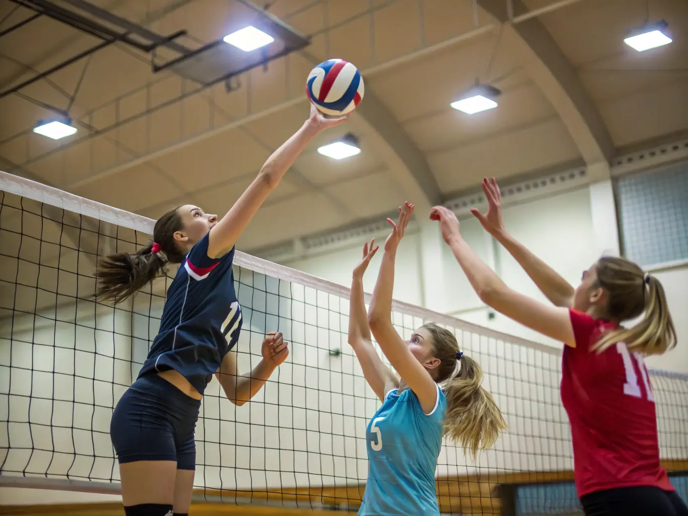A clean and spacious indoor volleyball court with members actively engaged in a game, demonstrating teamwork and sportsmanship under the supervision of a coach.